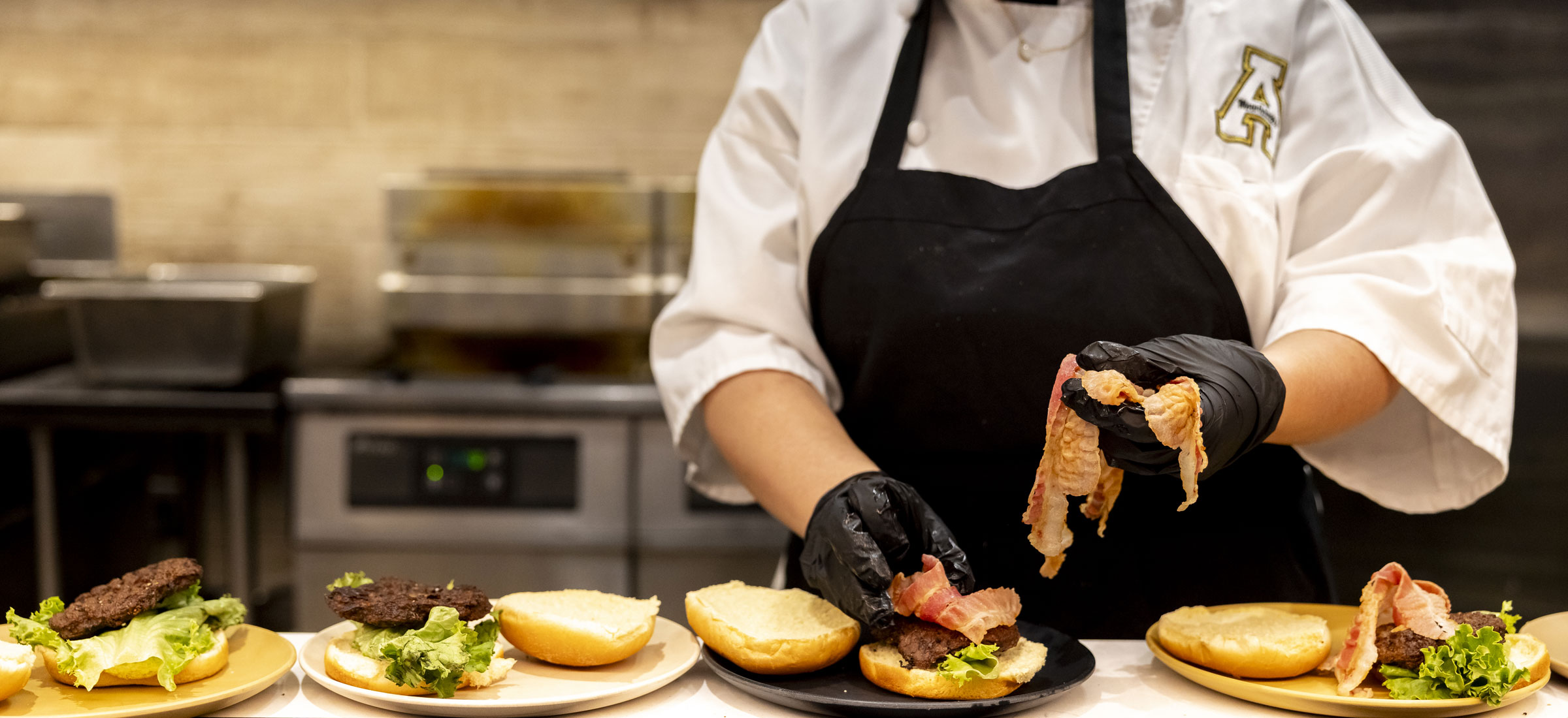 A chef or line cook is constructing multiple burgers simultaneously on a stainless steel counter