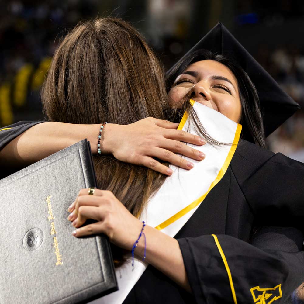 Faculty member and student hugging at commencement ceremony.